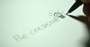 Close-up of handwritten 'Be creative' with a light bulb sketch on paper.